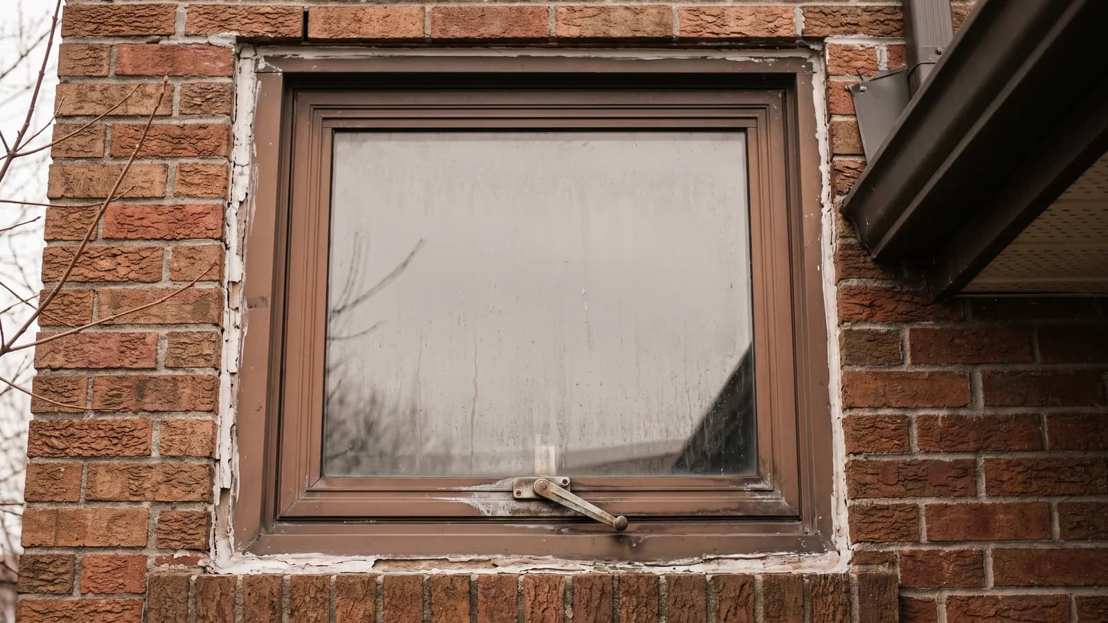 Original 1980s window on a brick home, worn frame and fogged glass